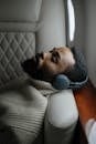 A relaxed man with wireless headphones sleeping on an airplane seat.